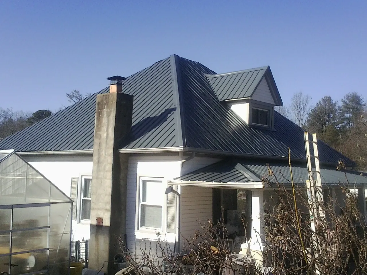 Dark blue standing seam metal roof on a white farmhouse with dormer — Slate & Tile Roof Repair by Roofing Brothers in Stratham