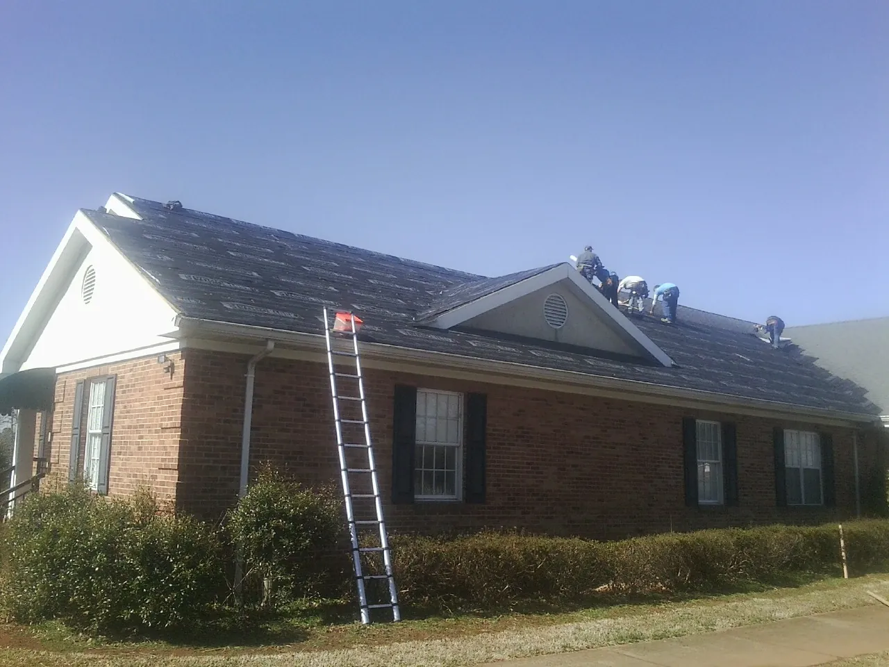 Crew tearing shingles off a brick ranch roof with a ladder set — Metal Roof Repair work by our crew in Stratham