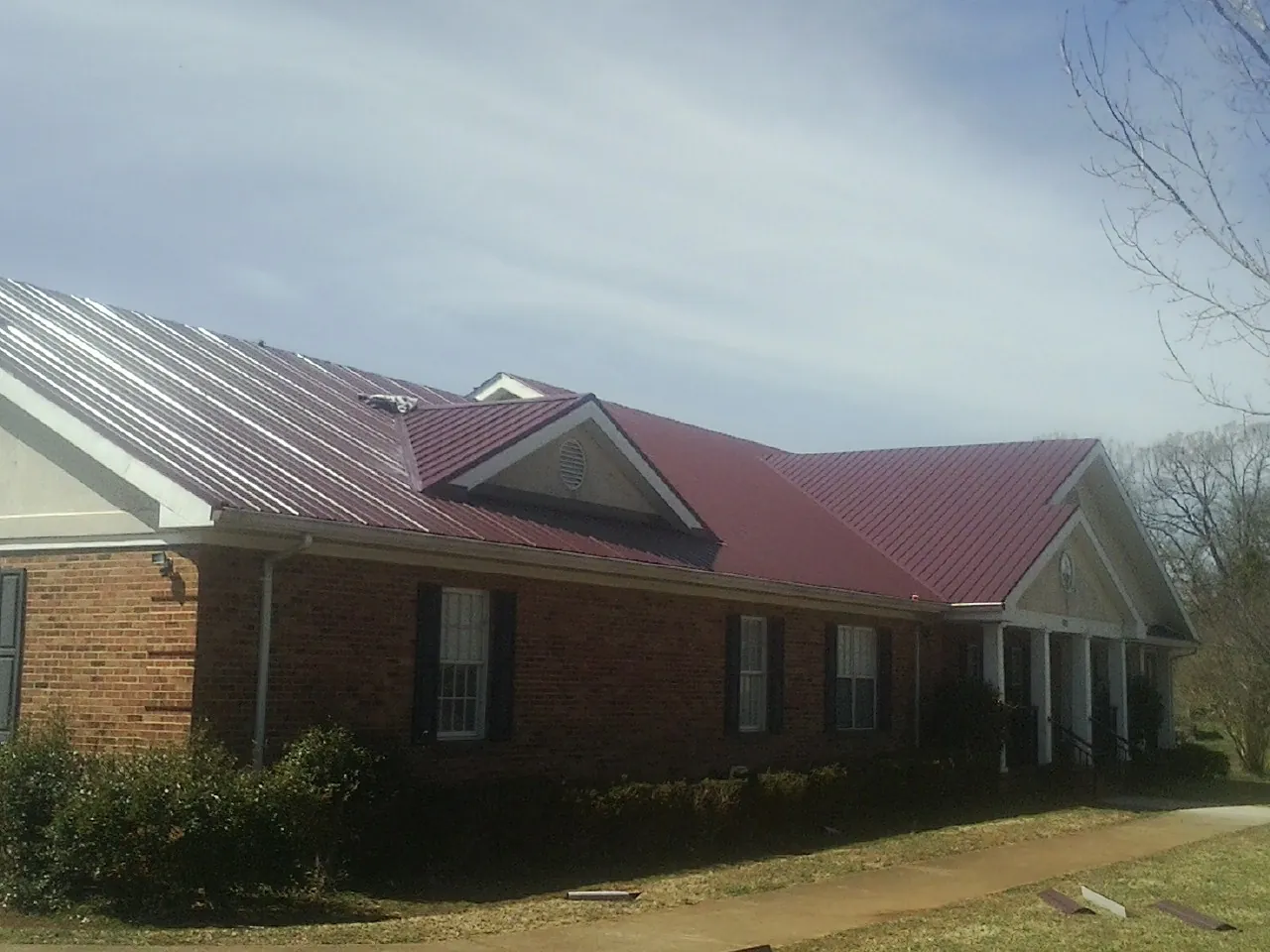 Red metal roof with gabled entries on a long brick building, from a Hail Damage Roof Repair job in Stratham
