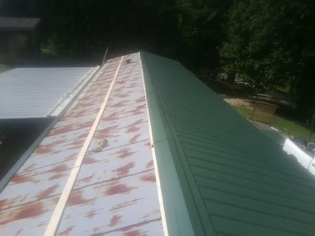Old rusted panels beside newly installed green metal roofing — Wind Damage Roof Repair by Roofing Brothers in Stratham
