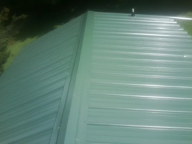 New green metal panels meeting at the ridge of a roof — Flat Roof Repair work by our crew in Stratham