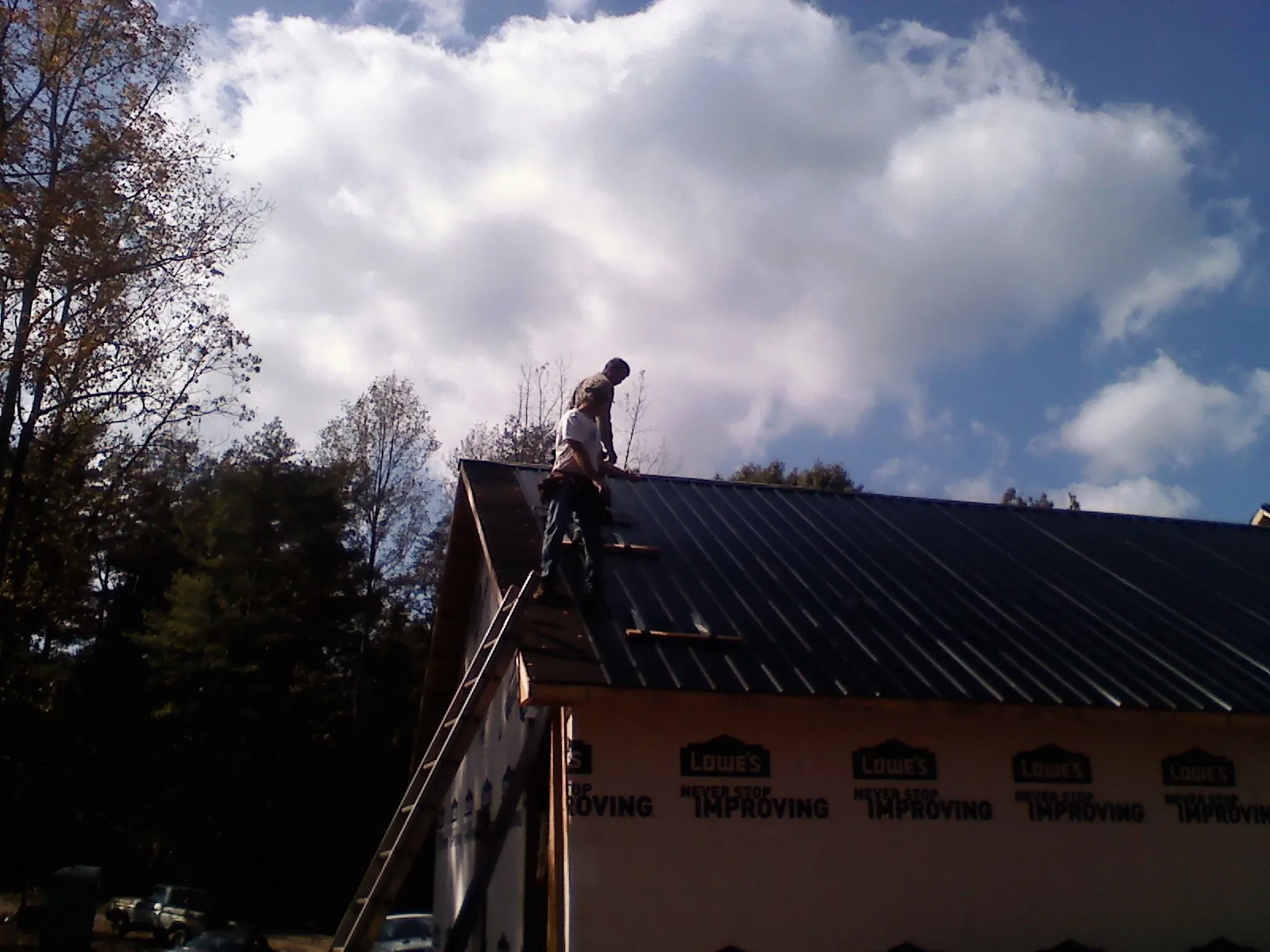 Roofer fastening dark metal panels high against a cloudy sky, from a Roof Inspection job in Stratham