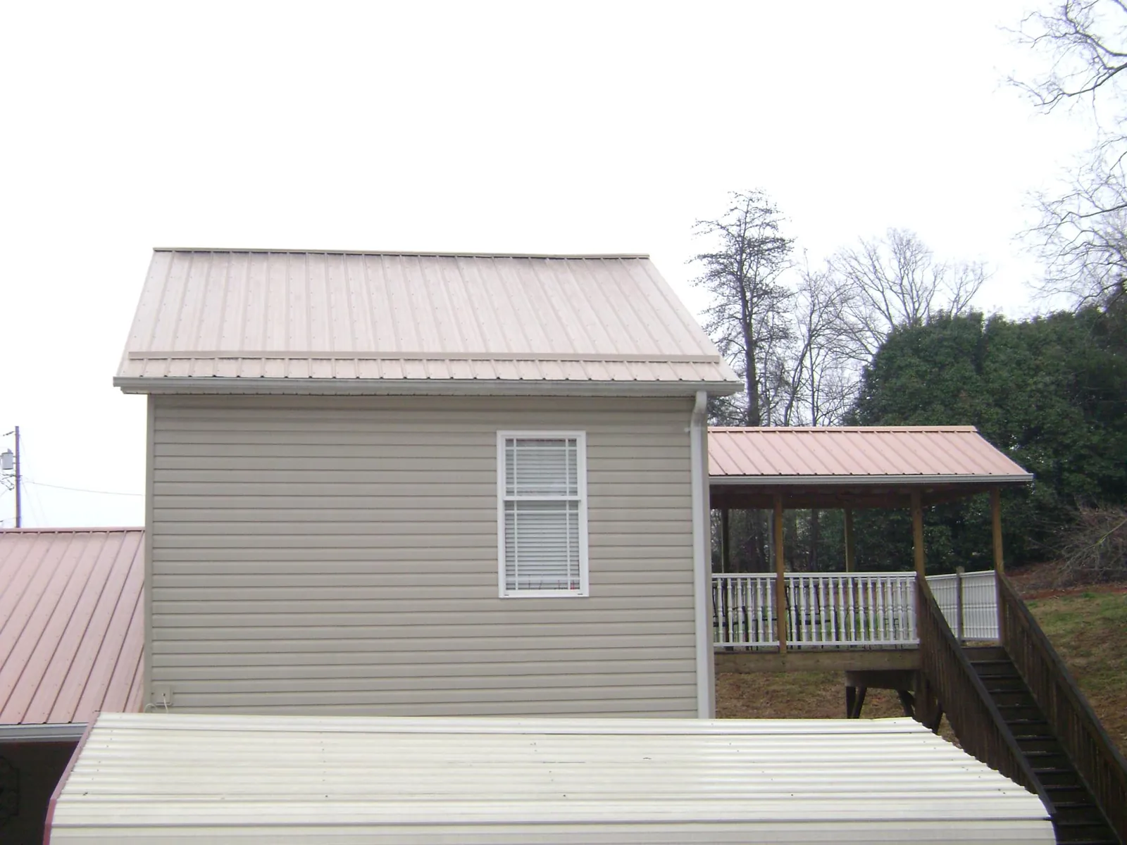 Tan metal roofs on a two story addition and attached porch, from a Roof Replacement job in Stratham